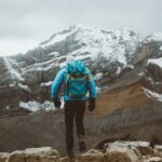 man in blue jacket and black pants standing on rock mountain during daytime