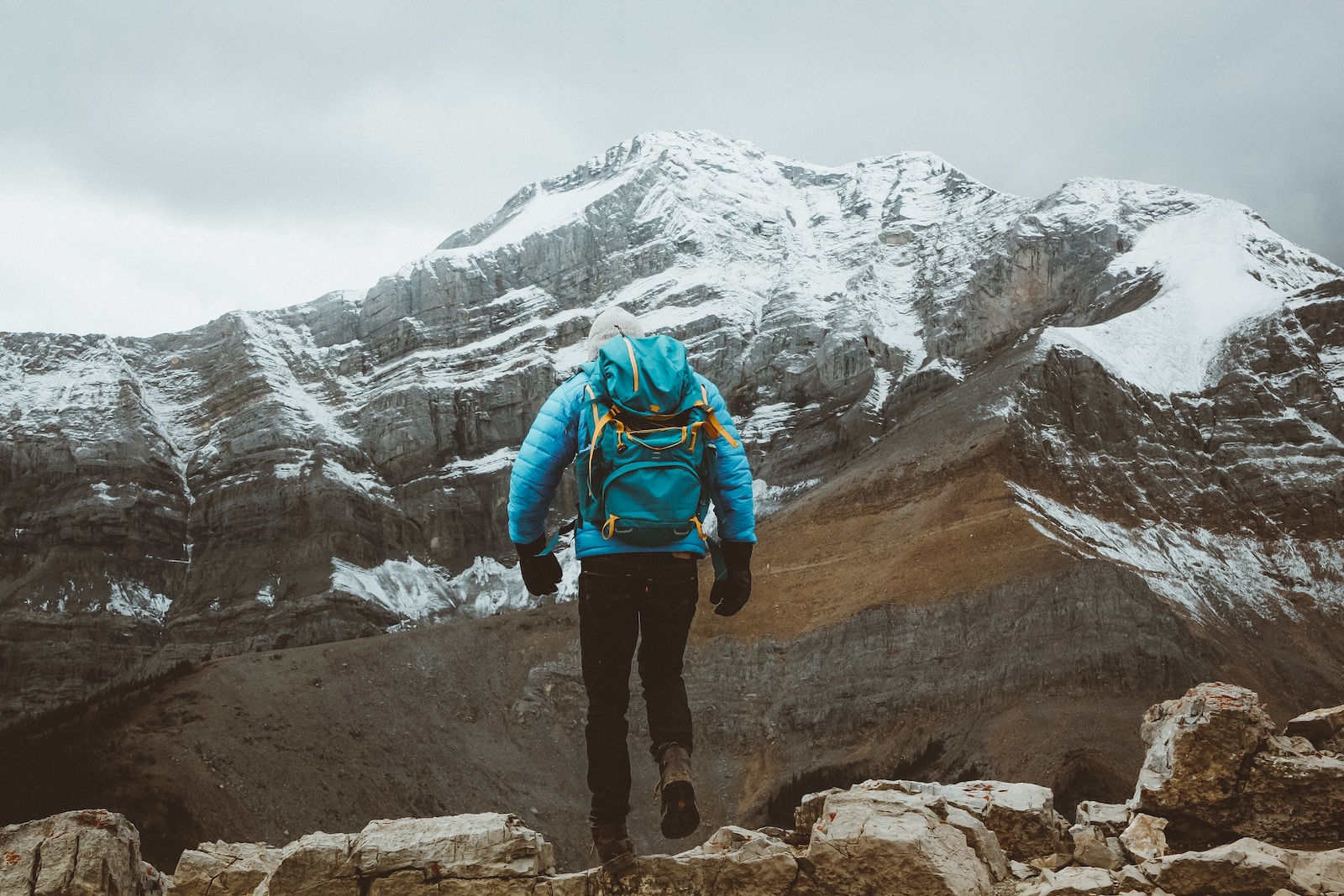 man in blue jacket and black pants standing on rock mountain during daytime